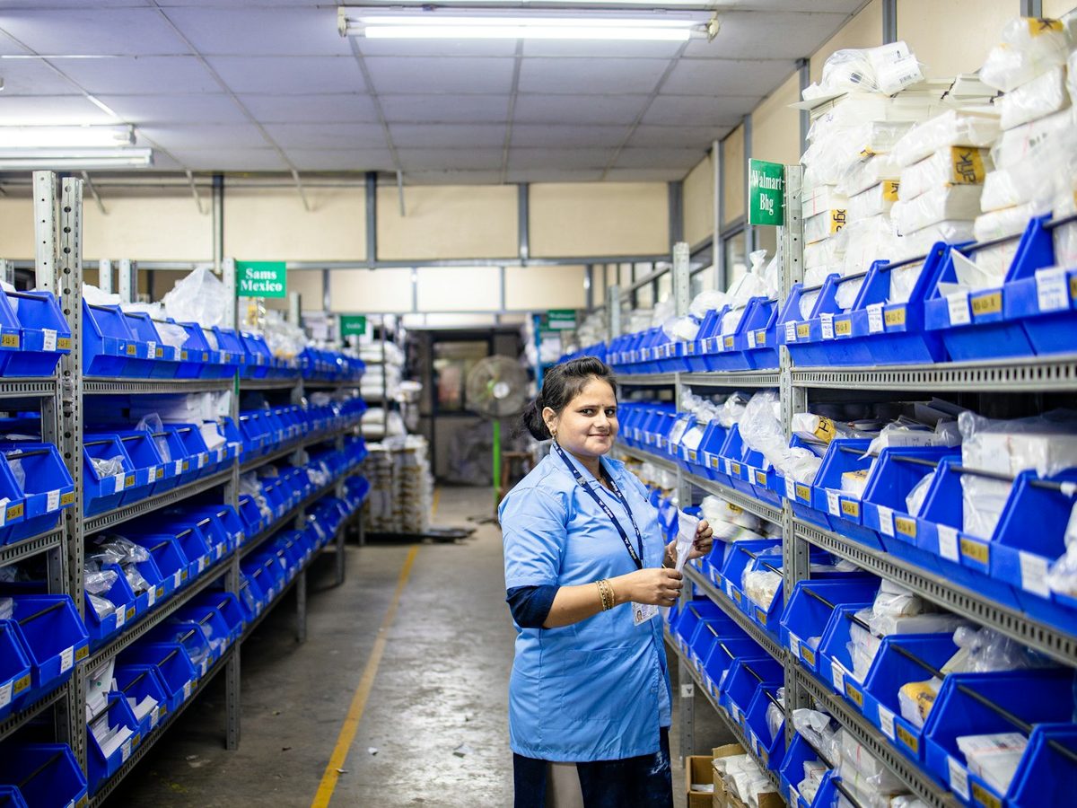 A member of staff checking stock in a warehouse aisle of blue picking bins.