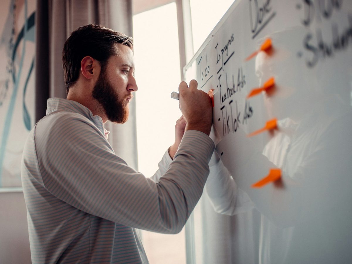 A man writing the week's plan on an office whiteboard.